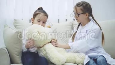两个可爱的孩子在玩泰迪熊。 熊病了。一个女孩是医生，检查<strong>毛绒熊</strong>。 另一个女孩是熊`